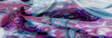 Koyu geometrik dokulara sahip bulanık bir kumaş ve beyaz çiçek aksanları, akışkan kıvrımlarla yumuşatılmış ve sanatsal bir dokunuş için ince mavi ve mor renklerle zenginleştirilmiş..