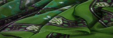 Çarpıcı mor geometrik desenler ve detaylı fırfırlar içeren koyu yeşil kumaş, canlı renklerin ve karmaşık dokuların harmanlanmış bir karışımını oluşturuyor.