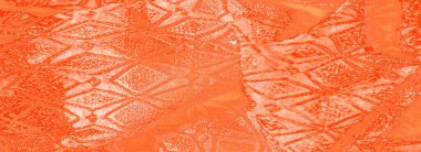 Bulanık turuncu kumaş pürüzsüz, yumuşak kıvrımlar ve karmaşık, parlak geometrik desen. Doku, ışığı yansıtan kumaşla çarpıcı bir detay ortaya çıkarıyor.