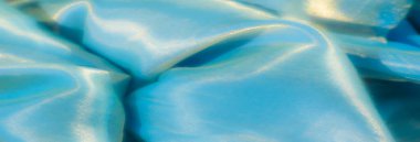 Yumuşak kırışıklıkları ve parlak ışık yansımaları olan parlak turkuaz bir kumaşın bulanıklığı, yaratıcı projeler için zengin dokusunu ve akışkan görünümünü vurguluyor.