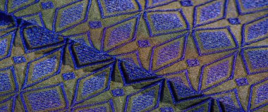 Görüntü, kumaşın tasarımı altın ve mavi elmas şekilli desenlerle zengin dokuyu birleştirerek lüks ve zarif bir estetik yaratıyor..