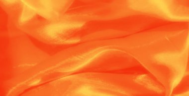 Işıldayan kıvrımları olan yumuşak turuncu kumaş bulanıklığı. Işık dokulu yüzeyle etkileşerek sıcaklık ve ışıldayan zarafet izlenimi yaratıyor..