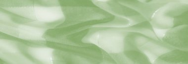 Birbirine dolanmış iplikler ve katmanlı dokularla sarmalanmış yeşil kumaşın bulanık sanatsal görüntüsü yumuşak, parıldayan bir görünüme ve soyut güzelliğe sahip dinamik bir görüntü yaratıyor..