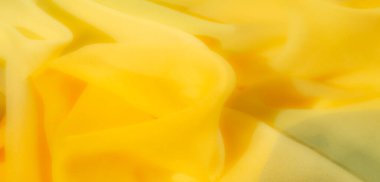 Bulanık - Sarı kumaş yumuşak dalgalarda zarifçe akıyor, sıcak ışıkla aydınlatılıyor. İnce kıvrımlar ve hassas doku onu arka plan ve tekstil tasarımları için ideal kılıyor..