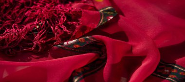 Bulanık kırmızı ve turuncu kumaş. Çiçekli ve soyut desenler ve ince altın detaylar. Katlanmış doku derinliği ve zarafeti arttırır..