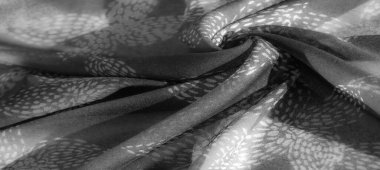 Görüntü. İnce bir dokusu olan gri pullu bir kumaş, bir yaprak ya da tüy tasarımına benzeyen soyut bir desen sergiliyor. Yüzeydeki ışık oyunu boyutsal bir görünüm yaratır.