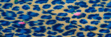 Mavi leopar benzeri desenli, bej bir yüzeyde pembe çiçekli kumaşın bulanık görüntüsü. Akan kıvrımlar zarif ve canlı bir görsel doku oluşturuyor..