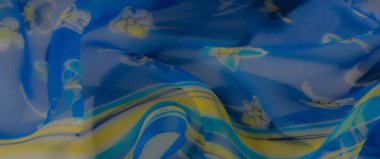 Yumuşak mavi kumaşı bulanıklaştırın, zarif bir şekilde sarı, turkuaz ve beyaz çiçek desenleriyle süsleyin. Akan kıvrımları hafif, havadar bir zarafet yayar..