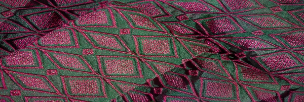 Yumuşak, yeşil bir kumaşın bulanık, pembe işlemeli hali. Kalıplı desen çarpıcı bir görsel yaratıyor, işçiliği ve modern tekstil tasarımını canlı renklerle vurguluyor..