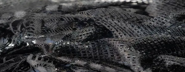 Siyah dantelli kumaşın bulanık soyut fotoğrafı. Karmaşık dokuma desenleri ve ışık yansımaları. Doku ve gölgenin dinamik etkileşimini yaratıyor..