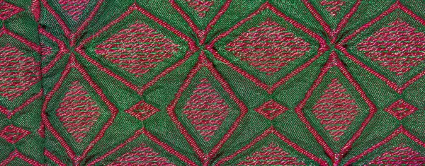 Karmaşık pembe ve yeşil geometrik desenler içeren renkli kumaşın bulanık görüntüsü. Kumaşın canlı renkleri ve detaylı tasarımı görsel olarak çarpıcı ve zengin bir kompozisyon yaratır..