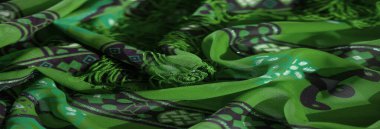 Mor geometrik desenleri ve hassas kenarları olan canlı yeşil kumaş bulanıklığı. Canlı zıtlıklar ve organik akışı yakalayan dokulu bir tekstil..