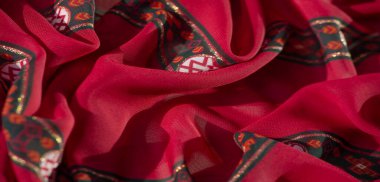 Kırmızı kumaştaki turuncu ve pembe renkli, karmaşık çiçek desenlerini bulanıklaştır. Canlı, sanatsal bir görünüş için yeşil ve parıltılı bir parıltı aksanları vardır..