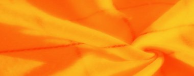 Dokulu turuncu ve sarı kumaş kıvrımlarının bulanık görüntüsü yumuşak ve pürüzsüz desenli ılık tonların ışıl ışıl bir bileşimini oluşturuyor..