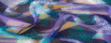 Işıldayan turkuaz desenlerle süslenmiş, yumuşak dokular ve gölgeler yaratmak için nazikçe katlanmış mor bir kumaşın yakın çekimi. Karmaşık detaylar ve canlı renkler uyum içinde harmanlanır.