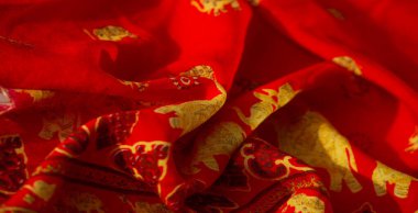 Görüntü, altın fil motifleri ve kalp şeklindeki desenlerin yer aldığı koyu kırmızı kumaşı vurguluyor. Geleneksel bir zarafet ve şenlik havası uyandırıyor..