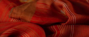 Işıl ışıl beyaz çizgili yumuşak turuncu kumaş ve çiçekli detaylar doğal ışık altında uyumlu bir doku ve tasarım dengesi oluşturmak için özenle katlanmış..