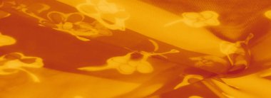 Nazikçe katlanmış turuncu kumaşlar çiçek aksanları, yumuşak dokuların parlayan ve dinamik bir bileşimini yaratmak için sıcak aydınlatma ile vurgulanır..