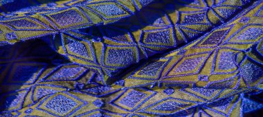 Mavi ve altın desenli bulanık yakın plan kumaş, parlak iplikler ve yumuşak kıvrımlarla tekrarlayan geometrik elmas deseni sergiliyor. Tekstil ve sanatsal projeler için mükemmel.