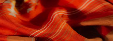 Bulanık görüntü, parlak turuncu kumaşı yumuşak, akışkan kıvrımlarla renklendiriyor. İnce çizgiler ve canlı çiçek desenleri doku ve estetik derinlik ekler..