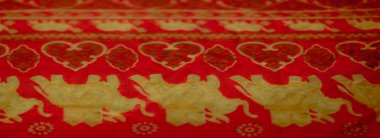 Altın fil ve çiçek desenleriyle süslenmiş parlak kırmızı kumaşın bulanık tasviri zengin kültür sanatını ve canlı renkleri vurguluyor..