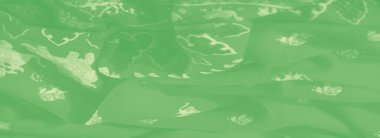 Yumuşak, bulanık yeşil kumaşlı, desenli ve çiçek desenli. Katlar organik bir akış yaratıyor. Kumaşa dinamik ama yumuşak bir görünüm veriyor..