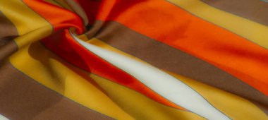 Bulanık - Sarı, turuncu, kahverengi ve kremin sıcak tonlu kumaş kumaş gölgeleri düz, saten benzeri dokusunu ve dinamik akışını vurgulayan spiral şeklinde bükülmüş.