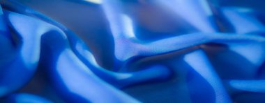 Bulanık, bu resim yumuşak mavi kumaşın güzel pürüzsüz kıvrımlarını detaylı bir şekilde gösteriyor. Karmaşık doku ve parıltı kumaşa derinlik ve boyut ekler ve zarafetini vurgular..