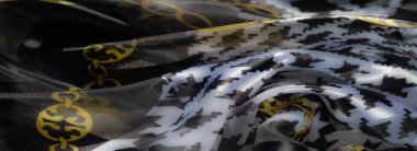 Canlı bir kumaşın bulanıklığı, altın zincir motifleriyle vurgulanmış siyah beyaz renkli cesur bir av köpeği deseni sergiliyor. Parlak yüzey büyüleyici bir görsel etki yaratır..