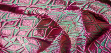 Çarpıcı pembe geometrik nakışlarla süslenmiş canlı yeşil bir kumaşın bulanık görüntüsü, pürüzsüz kıvrımlar ayrıntılı tasarımı ortaya çıkarıyor. Kumaş zengin yaratıyor.,