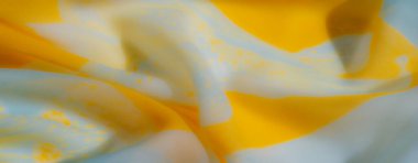 Sarı ve mavi kumaşın bulanık görüntüsü dinamik ve havadar bir düzende katlanır, yumuşak dokular ve büyüleyici soyut bir tasarım için canlı renkler.