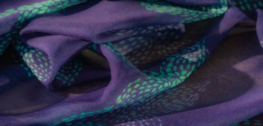 Narin deniz mavisi ve turkuaz noktalı mor bir kumaşın bulanık görüntüsü. Yumuşak kıvrımlar ve karmaşık detaylar sanatsal ve sofistike bir his yaratır..