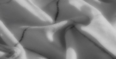 Gri tonlu kumaşın karmaşık çizgileri yumuşak kıvrımlarla buluşup büyüleyici bir tek renkli kompozisyonda uyumlu bir ışık ve doku dengesi yaratıyor..