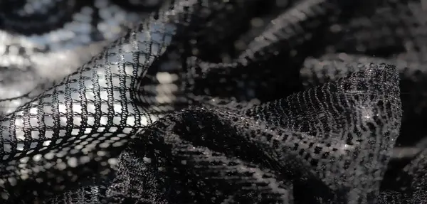 Karmaşık kıvrımlı siyah dantel parıldayan bir dokuyu yansıtır, tasarım veya dekorasyon için sanatsal ve lüks bir estetik yaratır..