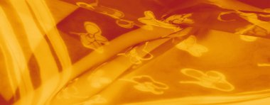 Yarı şeffaf dokusu olan altın sarısı kumaştan bulanık, ince dalgalar ve kıvrımlarla sıcak ve ışıltılı bir görüntü oluşturan narin çiçek desenleri sergiliyor..
