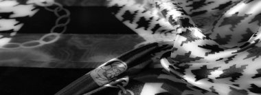 Görüntü. Pürüzsüz kıvrımlar ve ışık yansıtan ince dokularla geliştirilmiş karmaşık zincir desenleri ve geometrik tasarımları içeren bir dizi gri ölçekli kumaş görüntüler..