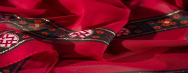 Turuncu ve yeşil aksanlı, çiçekli ve simetrik tasarımlı kırmızı kumaşın bulanık görüntüsü. Geleneksel ve modern sanatın mükemmel bir karışımı..