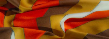 Kahverengi, sarı ve turuncu çizgilerden oluşan kıvrımlı, saten benzeri kumaş üzerinde bulanık bir etki. Her renk ince, ince mavi çizgilerle ayrılmış, samimi ve davetkar bir görünüm yaratıyor..