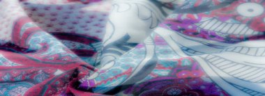 Beyaz çiçek motifleri, mor şal desenleri ve dinamik dokulara katlanmış karmaşık mavi ve kırmızı desenler içeren canlı bir kumaşın bulanıklığı..