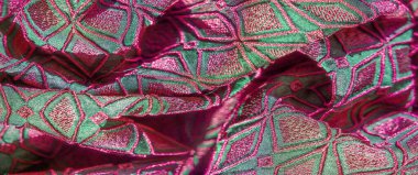 Pembe ve yeşilin canlı tonlarında geometrik desenli, dokulu bir kumaşın bulanık görüntüsü. Karmaşık nakış zengin ayrıntıları gösteriyor, lüks bir görünüm yaratıyor..