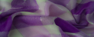 Canlı mor ve lavanta kumaştan bulanık. Parlayan iplikler, karmaşık dokular ve dinamik bir düzende yumuşak kıvrımlar..