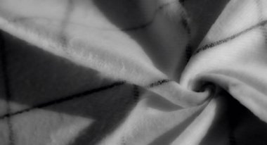 Yumuşak, katlanmış beyaz kumaşın bulanık yakın plan, ince siyah ızgara çizgileri var. Işık ve gölge dokuyu güçlendirir, zarif ve soyut bir görünüm yaratır..