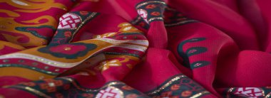 Turuncu ve kırmızı tonlarda çiçek ve geometrik desenli, altın aksanlı ve karmaşık siyah sınır detaylarıyla zenginleştirilmiş sanatsal bir kumaşın bulanıklığı..