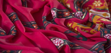 Görüntü güzel desenli kırmızı kumaşı ortaya çıkarır. Karmaşık turuncu ve koyu yeşil tonlarda çiçek ve geometrik tasarımlarla süslenir. Sanatsal yaratımlar için mükemmeldir..