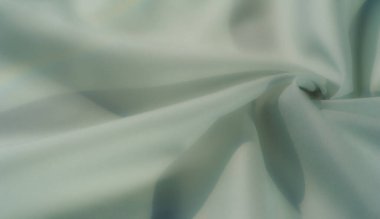 Görüntü, pürüzsüz katları ve yumuşak ışıkla aydınlatılmış pürüzsüz yüzeyleri olan zarif, yeşil bir kumaş. Artistik veya tasarım odaklı arka planlar için mükemmel rafine bir doku.