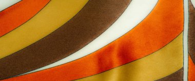 Parlak sarı, turuncu ve kahverengi çizgili kumaşlar, yumuşak kıvrımlı, lüks bir doku yaratıyor. Kalın renkler ve karmaşık desenler sıcaklık ve zarafet ekler..