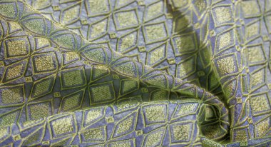 Yumuşak mavi bir kumaş üzerinde yeşil elmas şekilleri vurgulayan karmaşık altın işlemeli bulanıklık, dekor veya moda tasarımı için zengin ve zarif bir estetik sunar.
