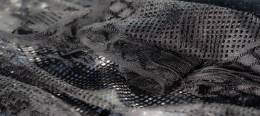 Parıldayan desenleri ve yumuşak kıvrımları olan siyah dantel kumaşın bulanık görüntüsü bu karmaşık tekstilin lüks ve ayrıntılı sanatını gözler önüne seriyor..