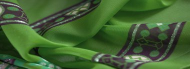 Karmaşık çiçek motifleri ve canlı mor aksanlı katlanmış yeşil kumaşın bulanık fotoğrafı. Katmanlı püsküller, tekstilin zenginliğini ve inceliğini arttırır..