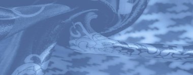 Pürüzsüz mavi kumaşın bulanık kıvrımları karmaşık houndstooth motiflerini zincir elementlerle göstererek klasik desenler ve çağdaş tasarımın bir karışımını sunuyor..